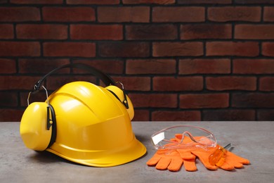 Photo of Hard hat, protective gloves, earmuffs, goggles and screwdriver on grey surface. Space for text