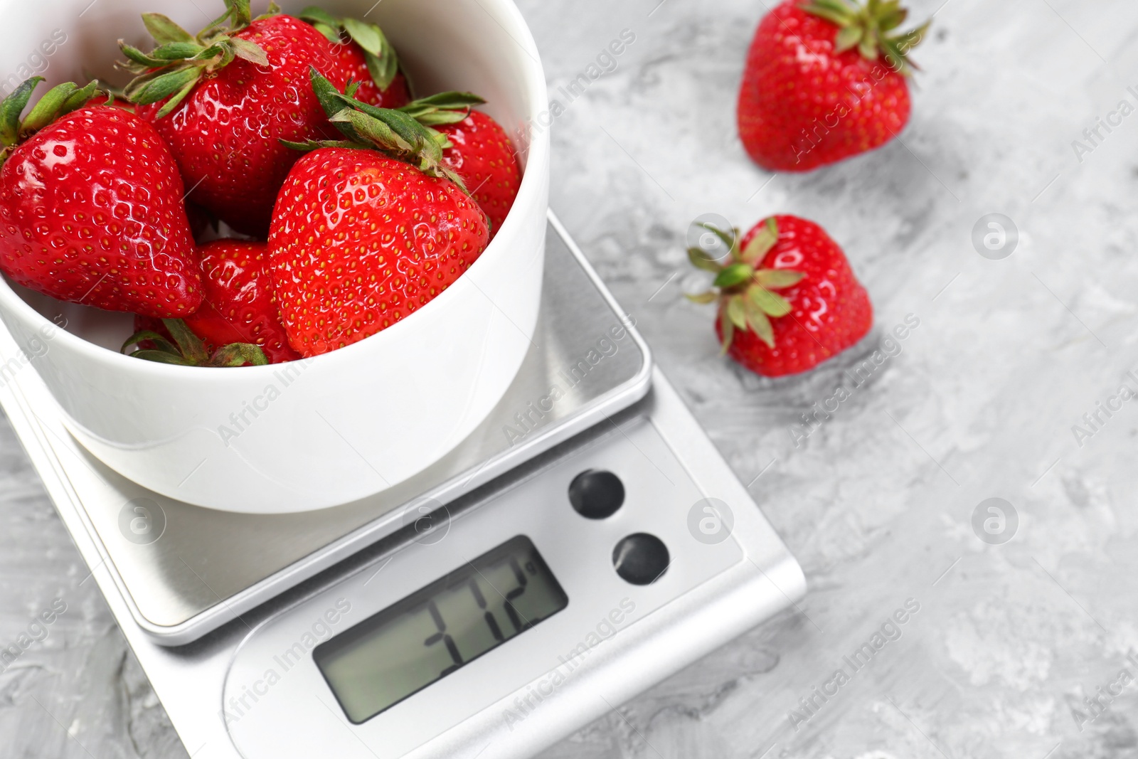 Photo of Kitchen scale with bowl of strawberries on grey textured table, closeup