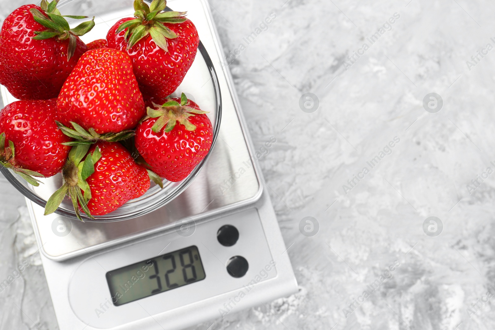 Photo of Kitchen scale with bowl of strawberries on grey textured table, top view. Space for text