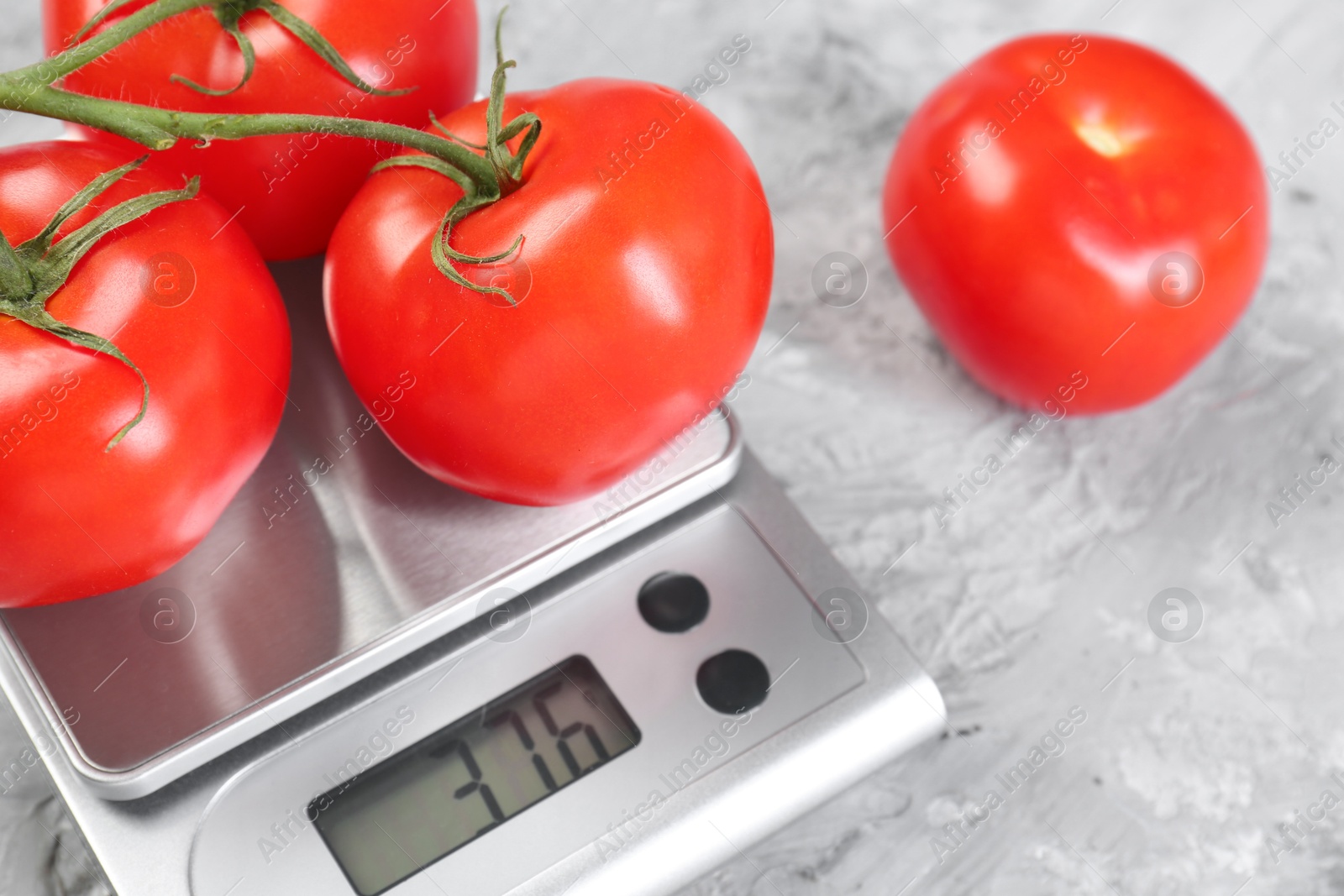 Photo of Kitchen scale with tomatoes on grey textured table, closeup