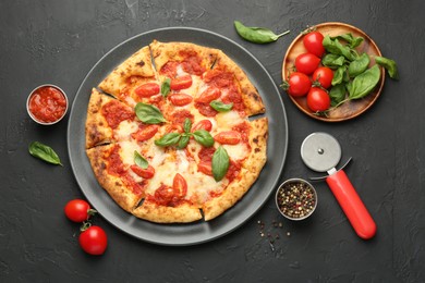 Photo of Delicious Margherita pizza, ingredients and cutter on black table, top view