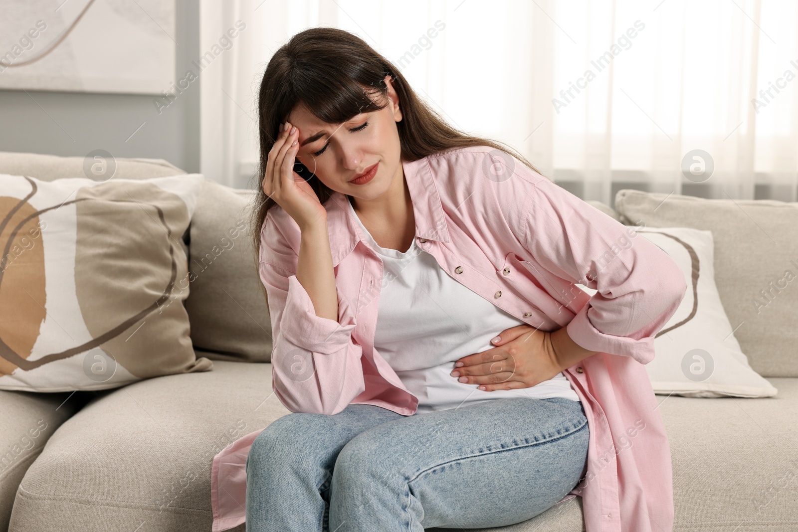 Photo of Upset woman suffering from abdominal pain on sofa at home