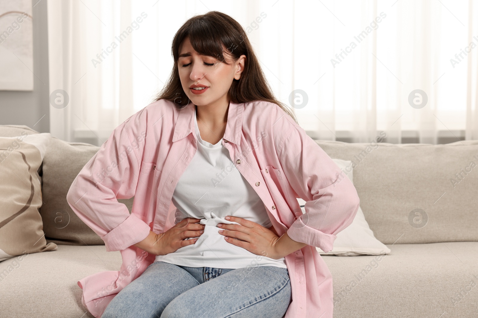 Photo of Upset woman suffering from abdominal pain on sofa at home