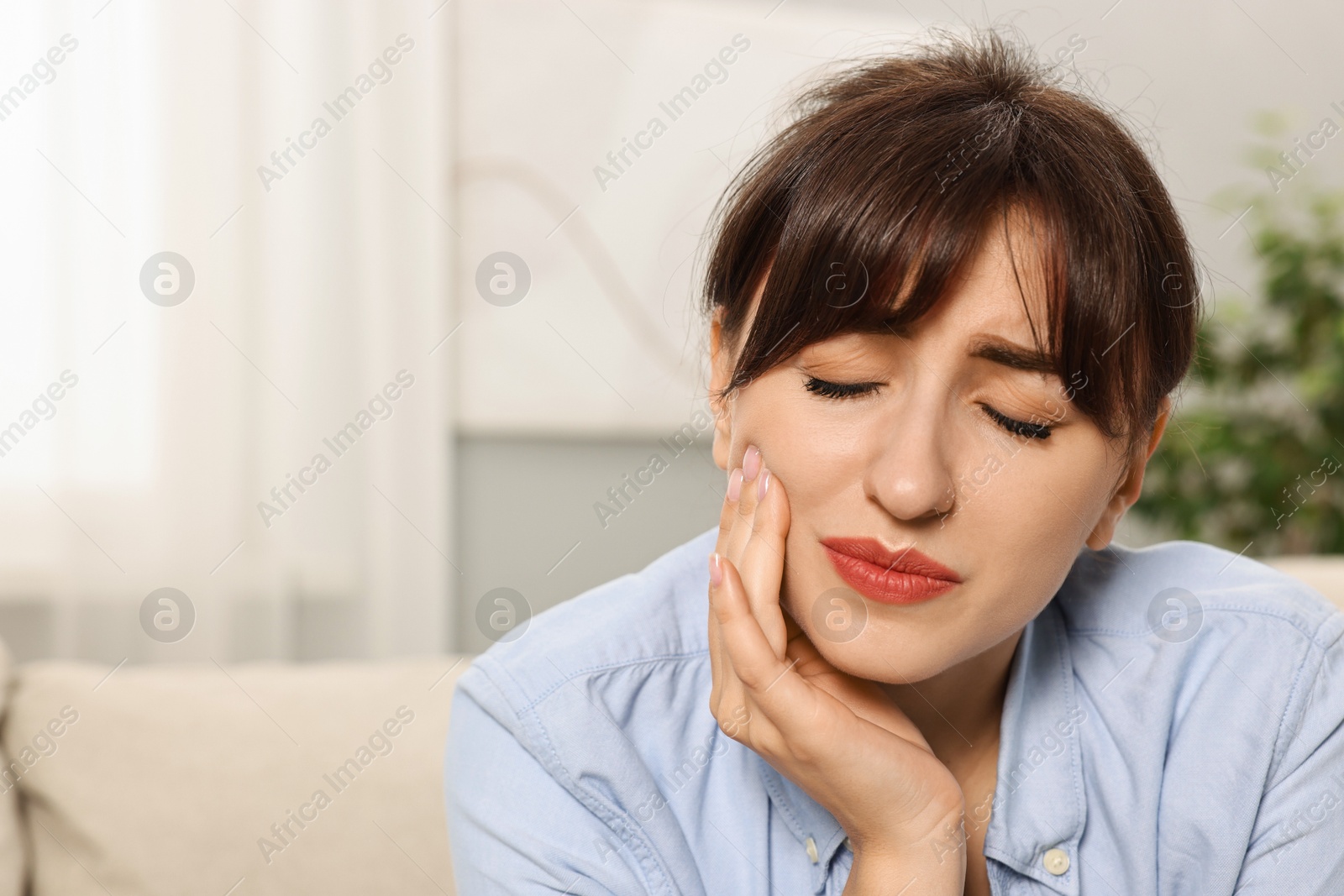 Photo of Upset young woman suffering from toothache indoors, space for text