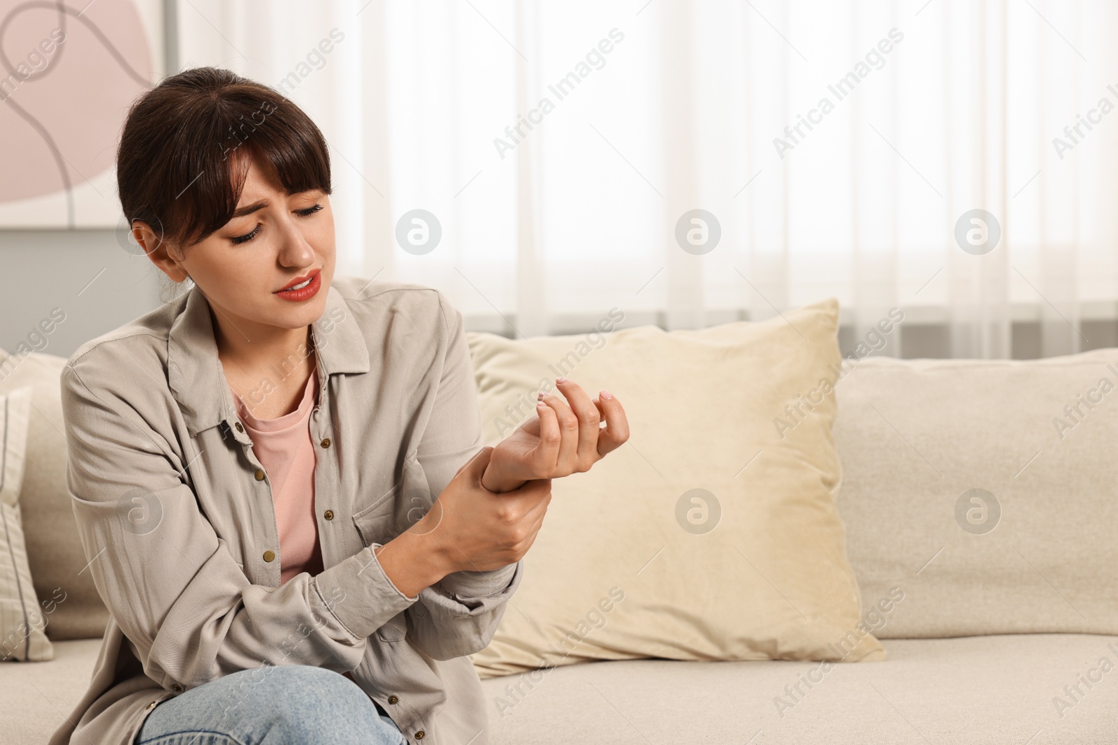 Photo of Upset woman suffering from pain in wrist on sofa at home, space for text