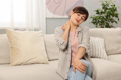 Photo of Upset woman suffering from neck pain on sofa at home
