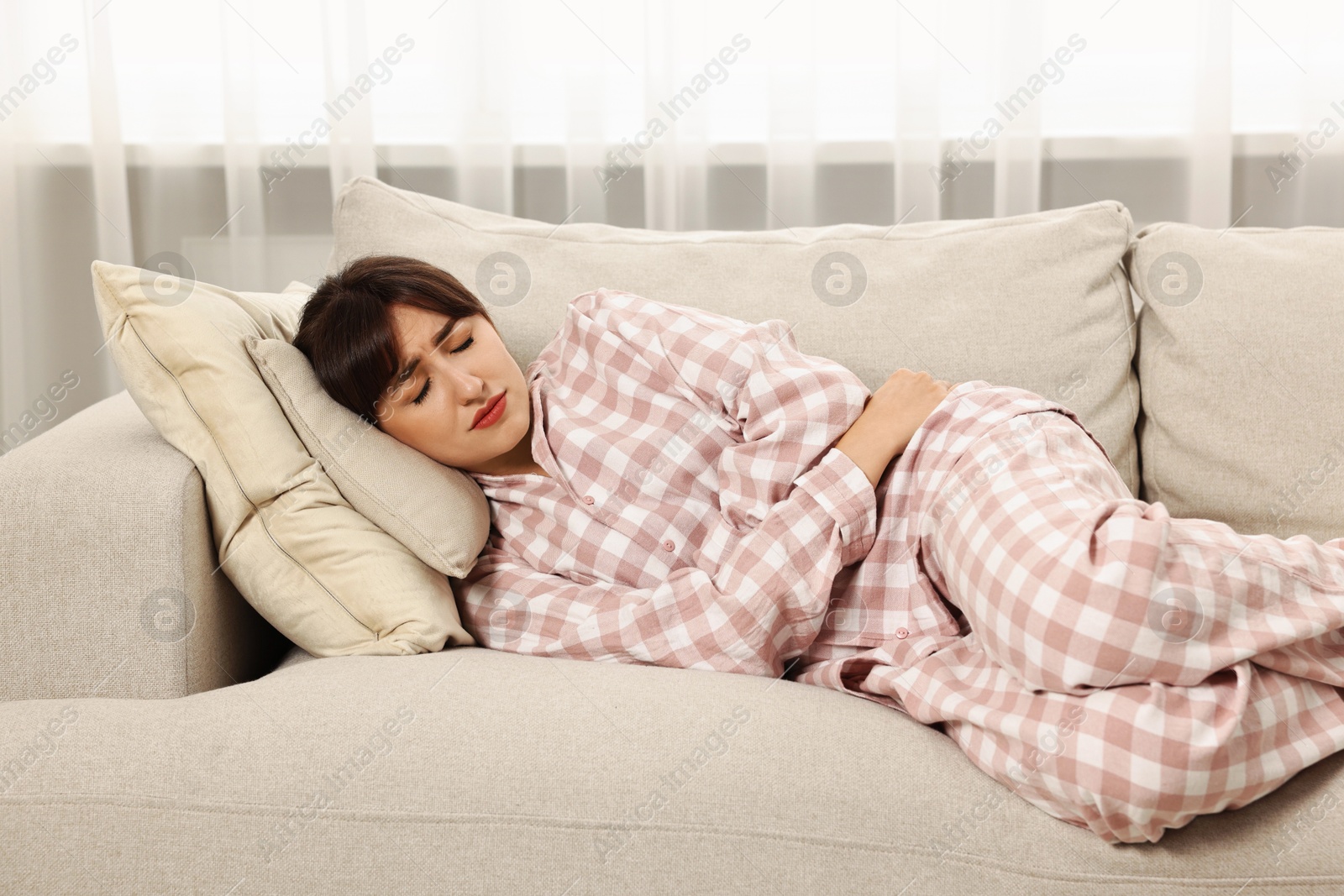 Photo of Upset woman suffering from abdominal pain on sofa at home