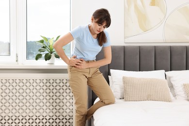 Photo of Upset woman suffering from hip joint pain in bedroom
