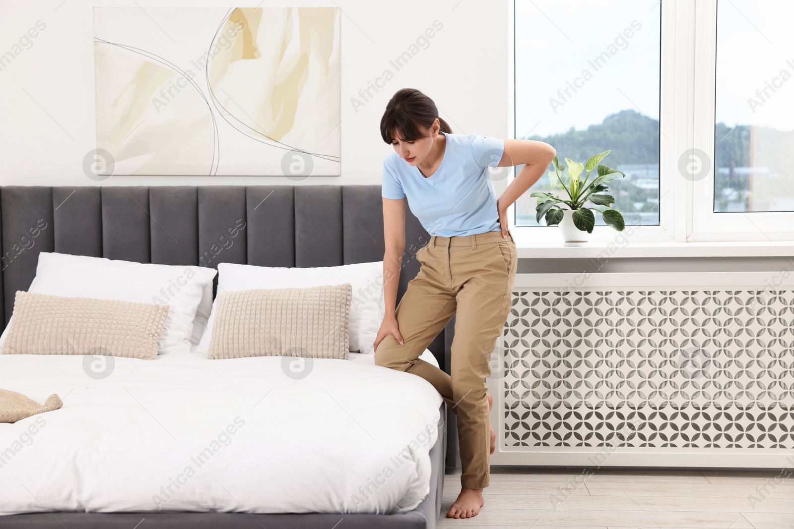 Photo of Upset woman suffering from back pain in bedroom