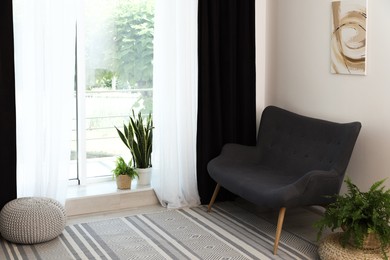 Photo of Sofa, green houseplants, pouffe and elegant curtains in room. Interior design