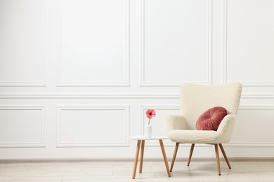 Soft armchair and coffee table with flower in stylish room. Space for text