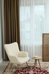 Photo of Soft armchair, coffee table and window with curtains in room. Interior design