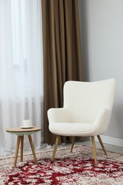 Photo of Soft armchair, coffee table and window with curtains in room. Interior design