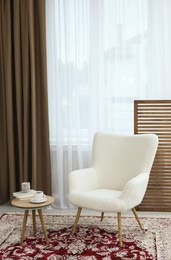 Photo of Soft armchair, coffee table and window with curtains in room. Interior design