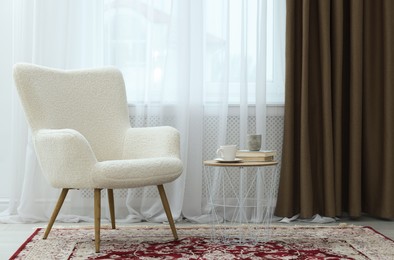 Photo of Soft armchair, side table and window with curtains indoors. Interior design