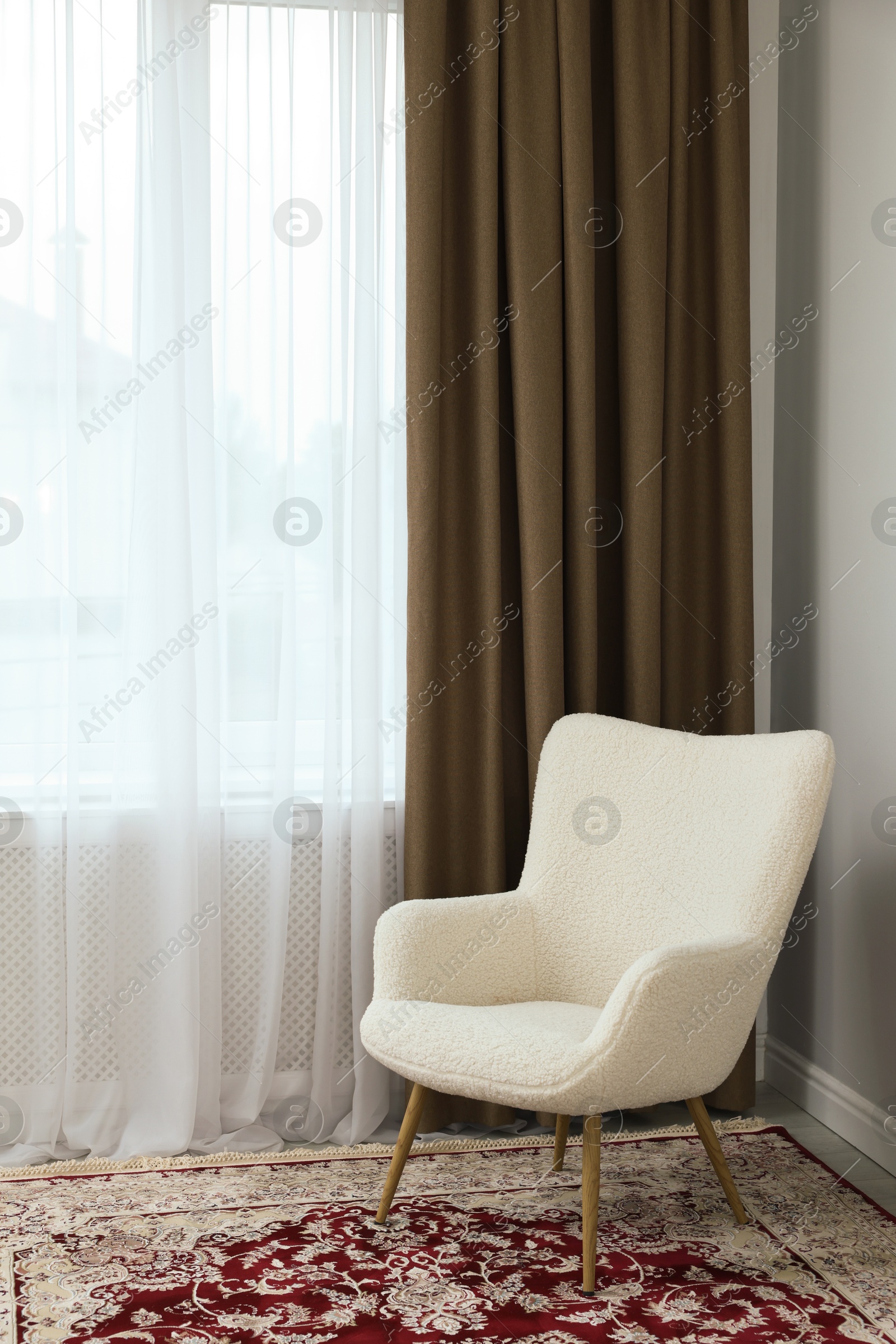 Photo of Soft armchair near window with curtains indoors. Interior design