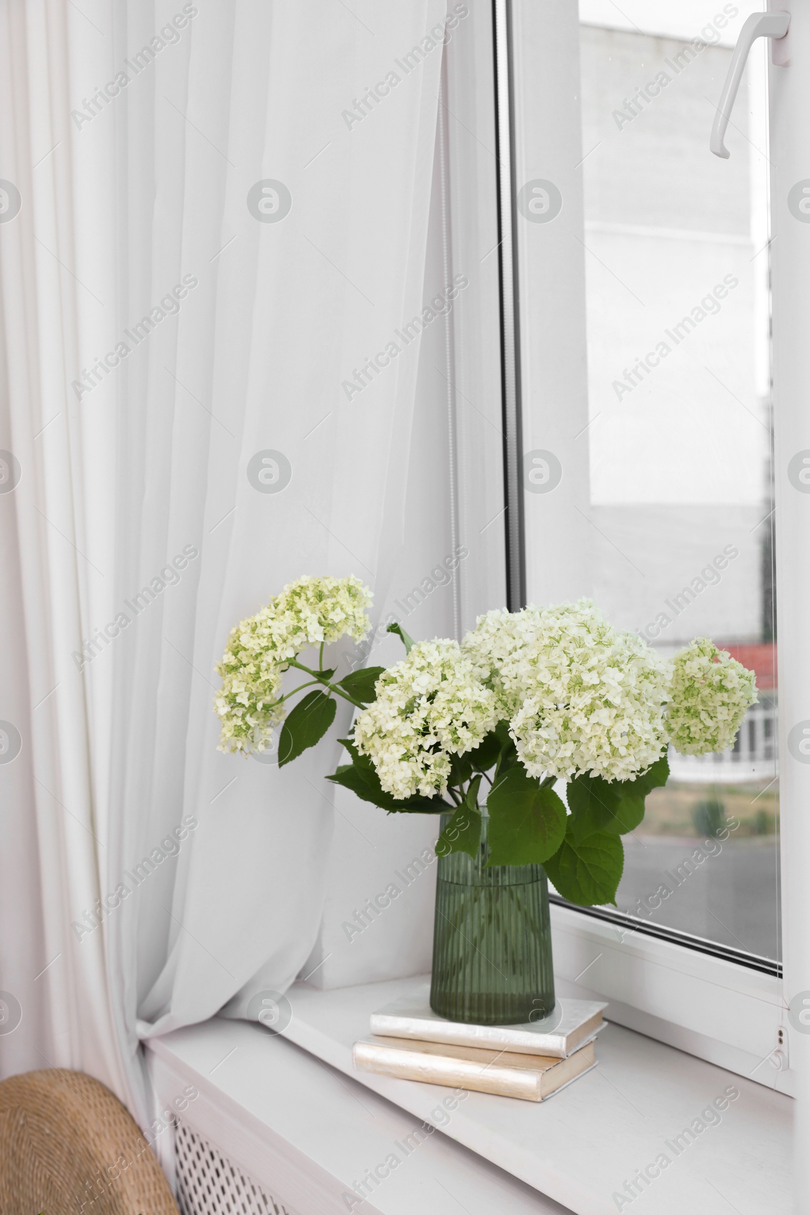 Photo of Beautiful flowers in vase and stack of books on window sill indoors