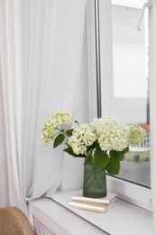 Photo of Beautiful flowers in vase and stack of books on window sill indoors