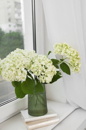 Photo of Beautiful flowers in vase and stack of books on window sill indoors