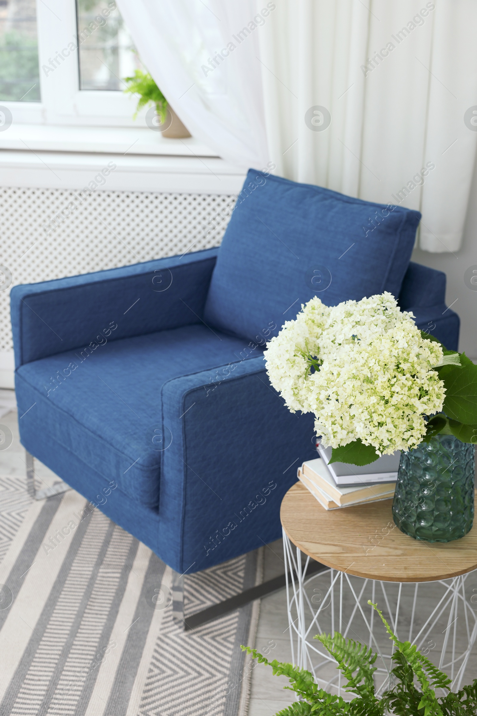 Photo of Soft armchair, side table, flowers and books indoors