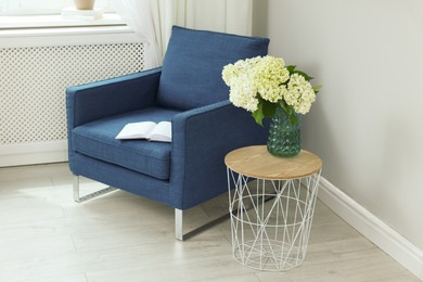 Soft armchair, book, side table and flowers indoors