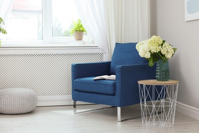 Photo of Soft armchair, side table, flowers and window with curtains in room. Interior design