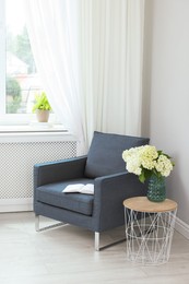 Photo of Soft armchair, side table, flowers and window with curtains in room. Interior design