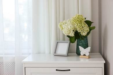 Photo of Chest of drawers, flowers, decorative elements and window with curtains indoors. Space for text