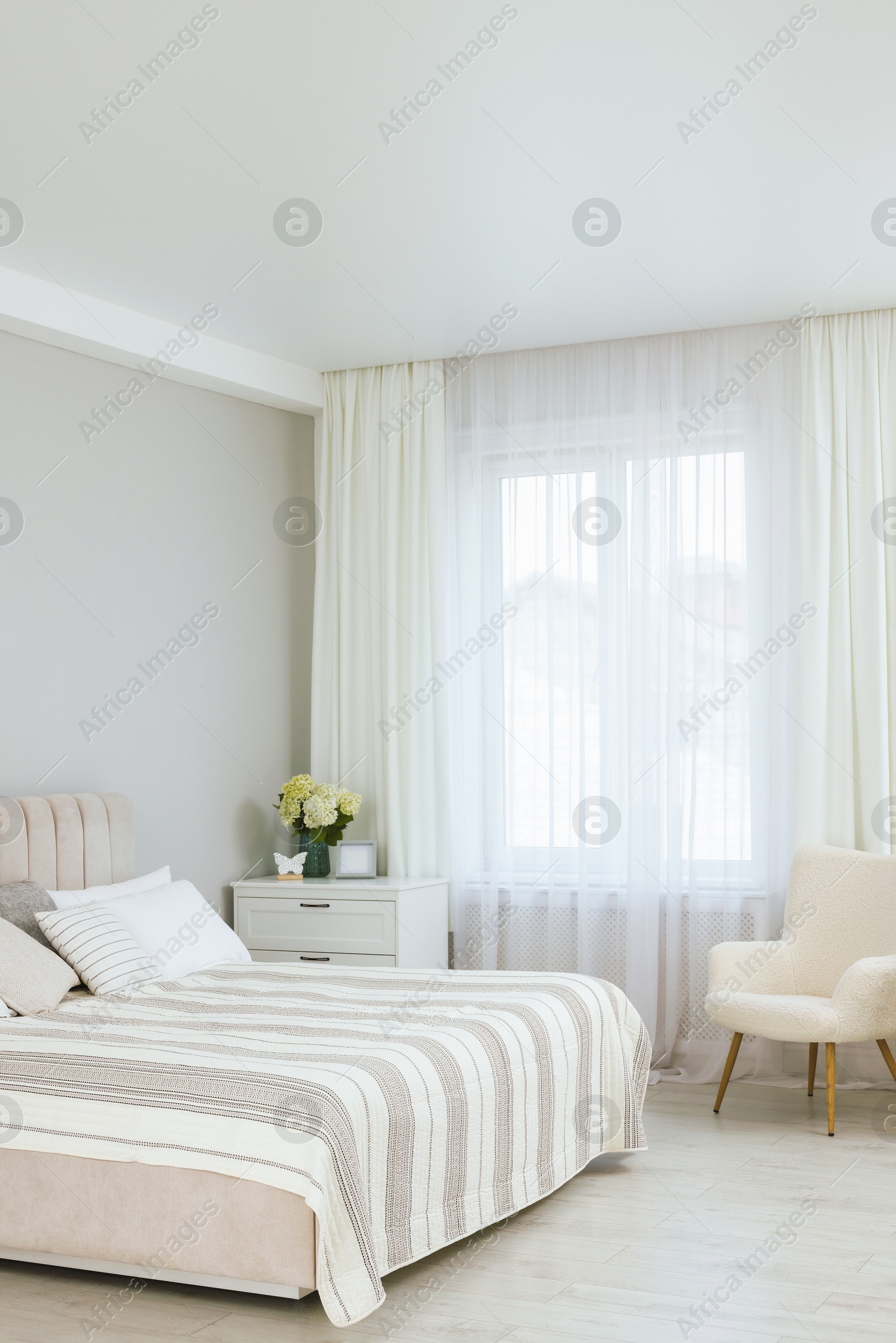 Photo of Large bed, chest of drawers, armchair and window with curtains in bedroom. Interior design