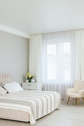 Photo of Large bed, chest of drawers, armchair and window with curtains in bedroom. Interior design