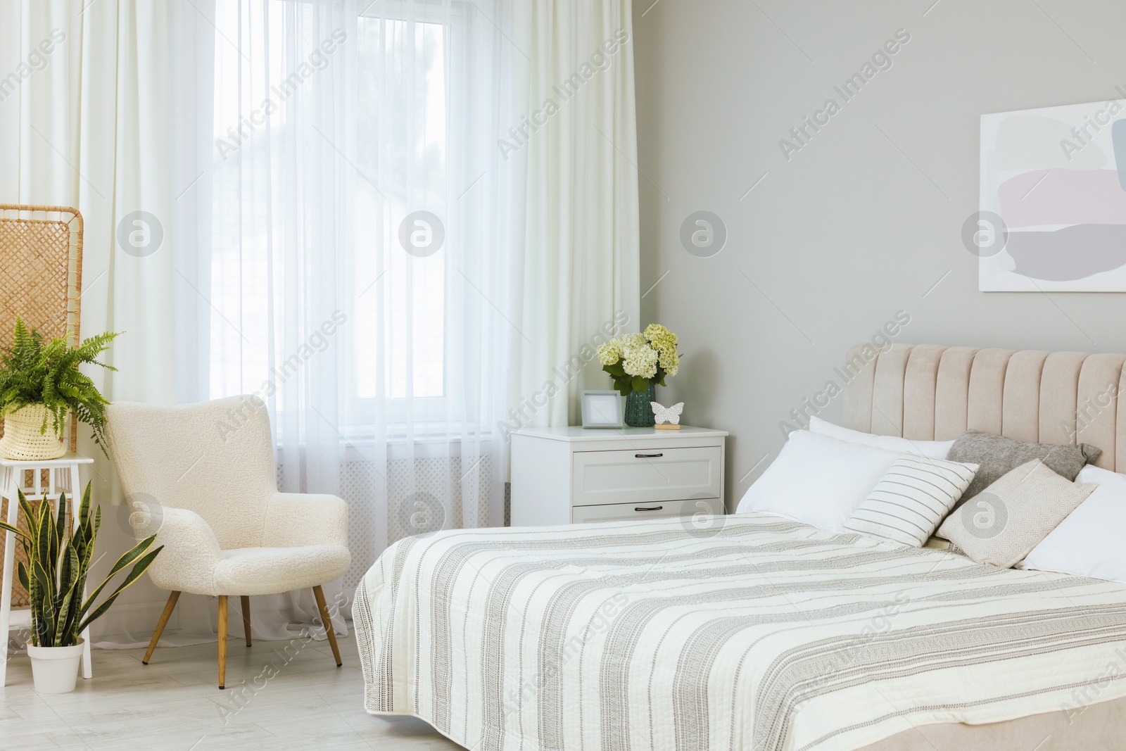 Photo of Large bed, chest of drawers, armchair, houseplants and window with curtains in bedroom. Interior design