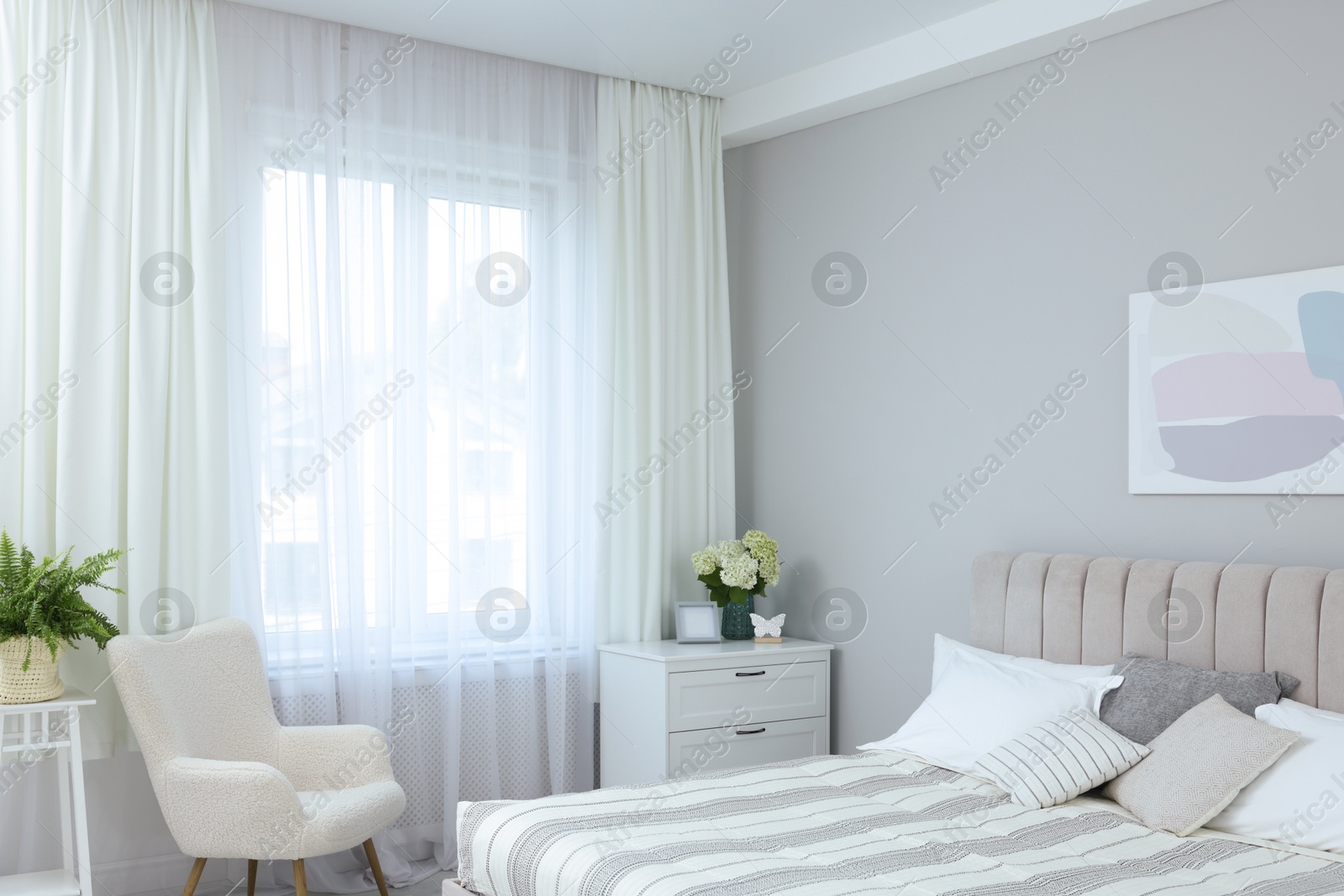 Photo of Large bed, chest of drawers, armchair and window with curtains in bedroom. Interior design