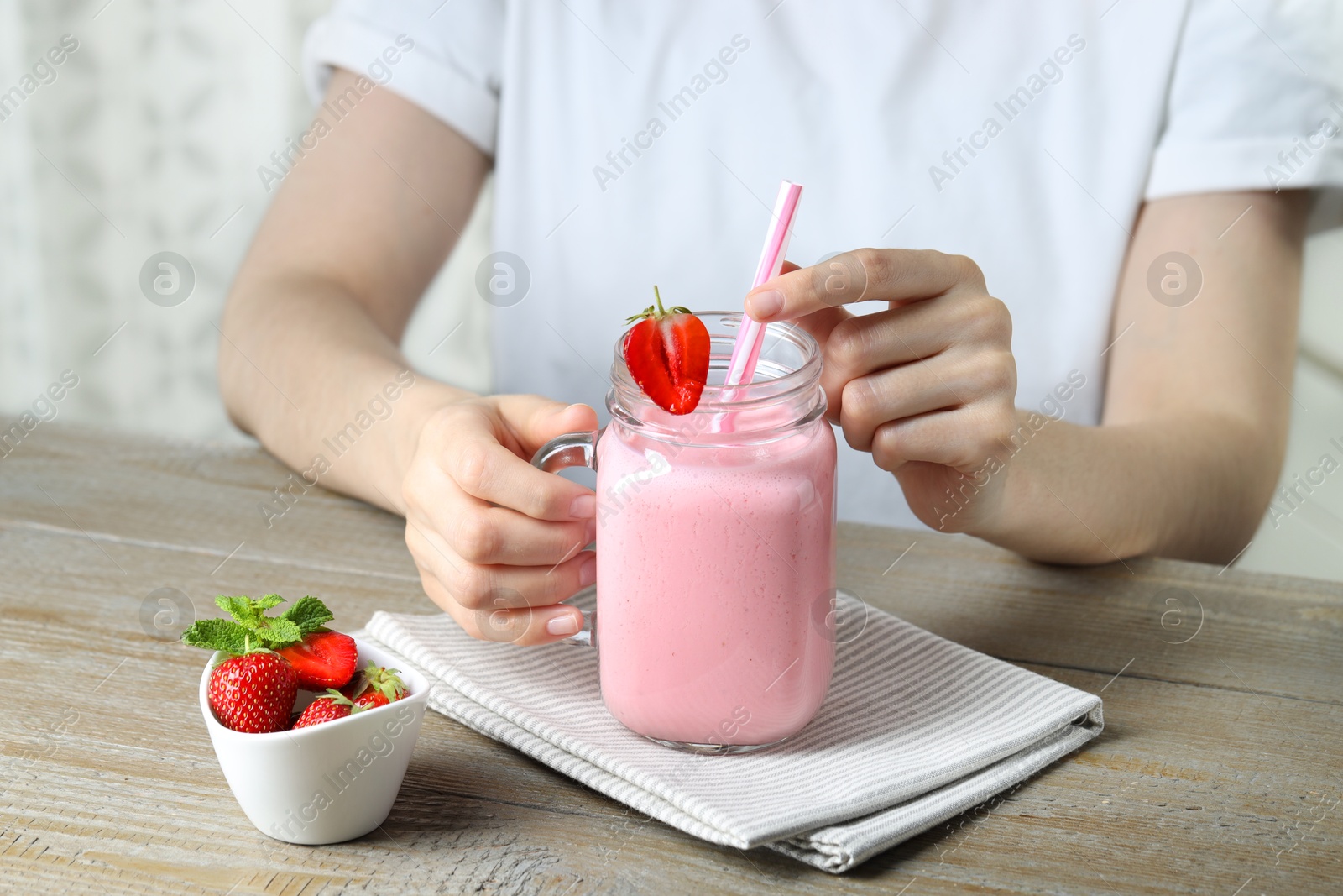 Photo of Woman with mason jar of tasty strawberry yogurt at wooden table, closeup