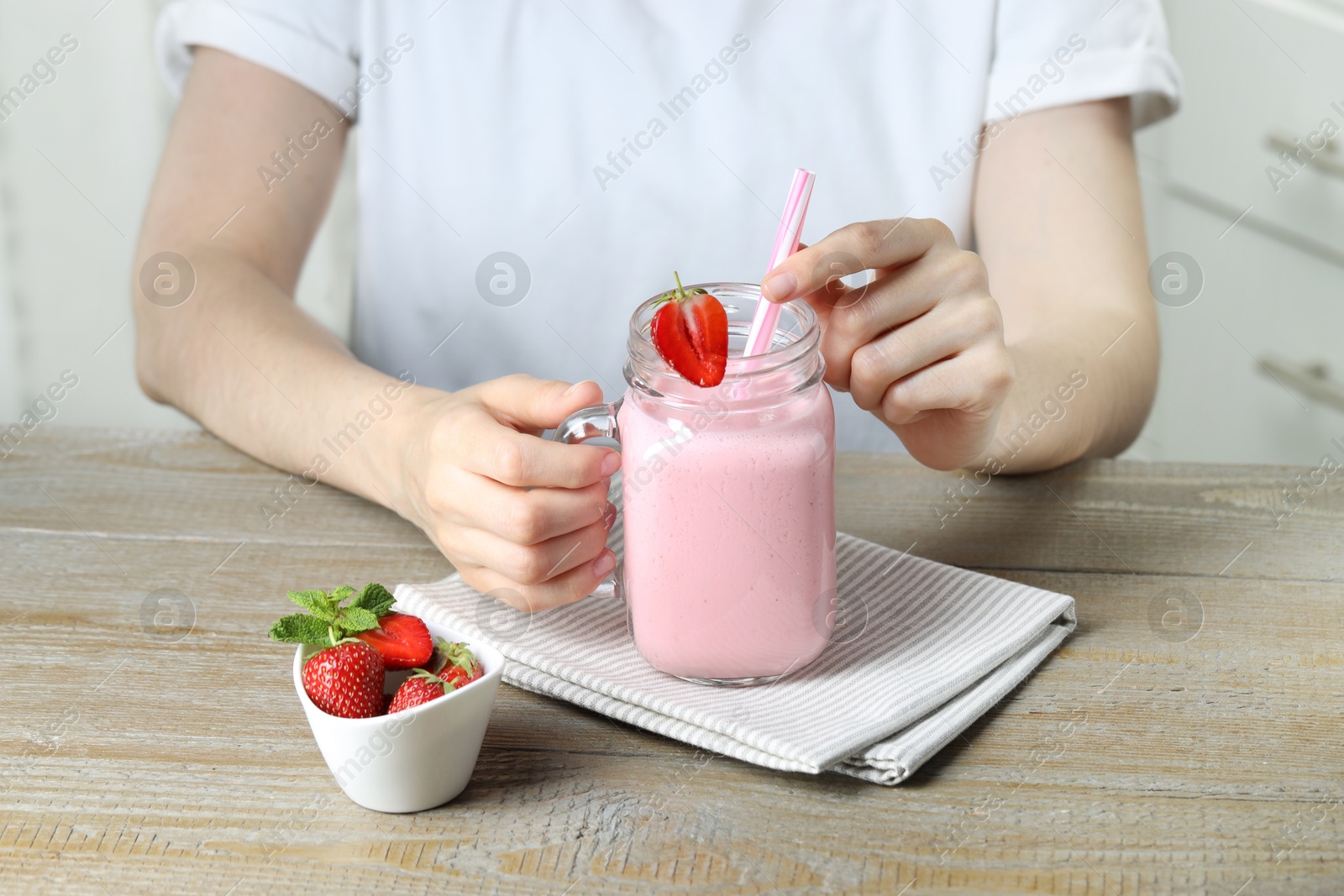 Photo of Woman with mason jar of tasty strawberry yogurt at wooden table, closeup