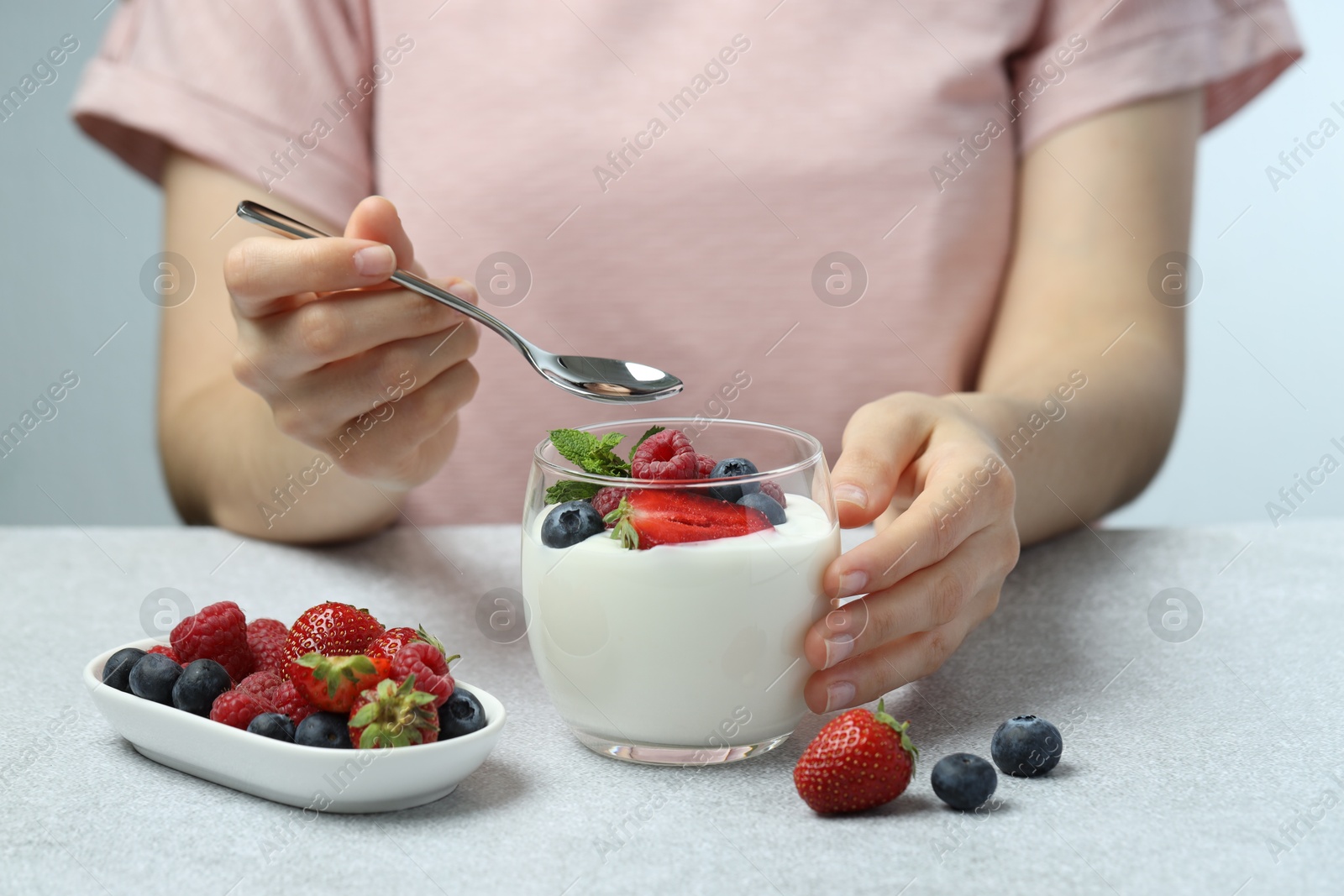 Photo of Woman eating tasty yogurt with fresh berries at light gray textured table, closeup