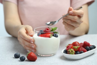 Photo of Woman eating tasty yogurt with fresh berries at light gray textured table, closeup