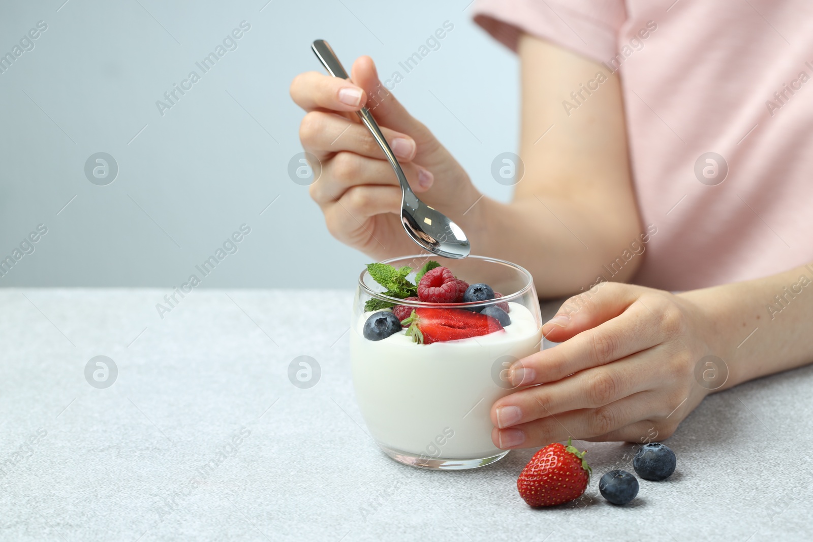 Photo of Woman eating tasty yogurt with fresh berries at light gray textured table, closeup. Space for text