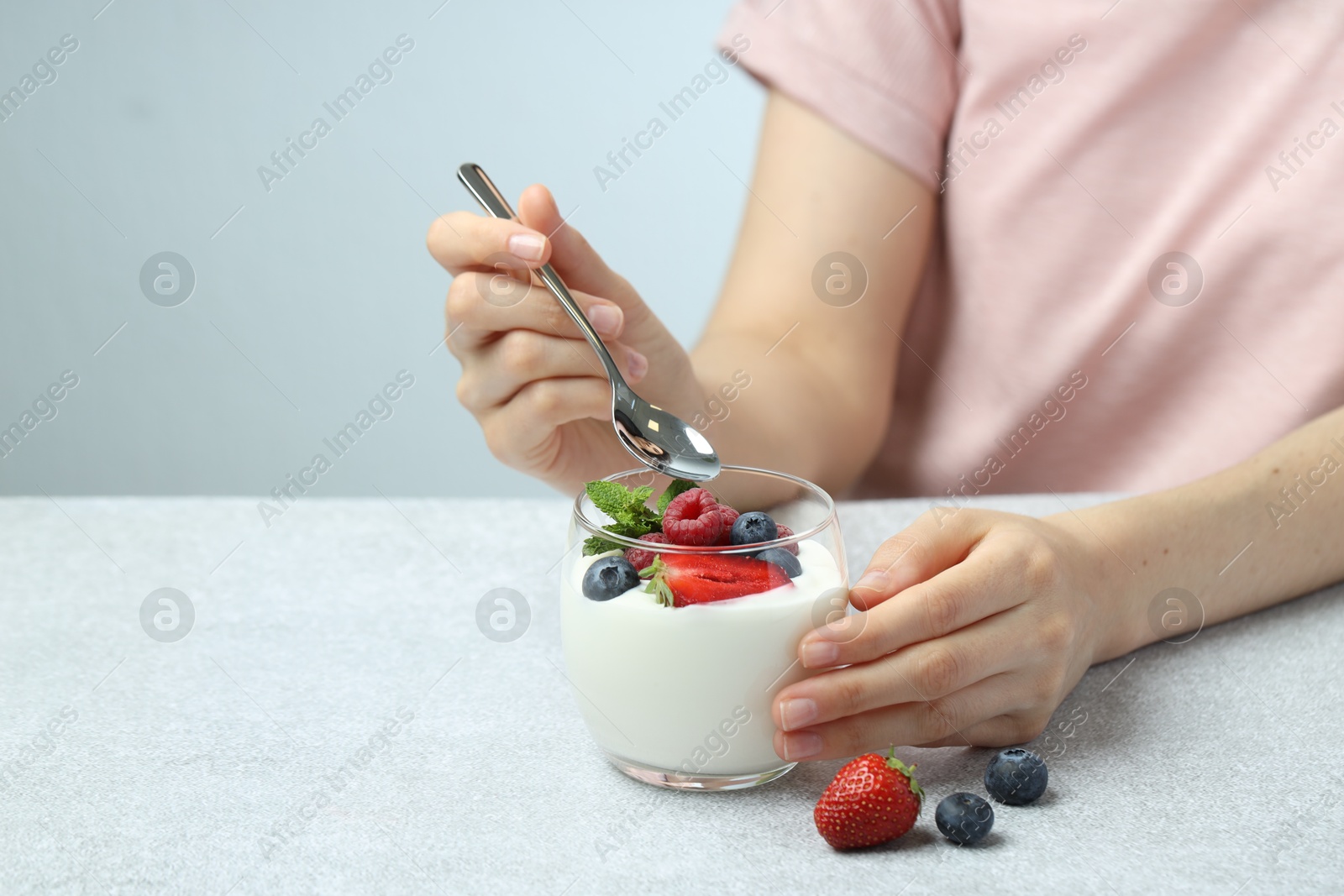 Photo of Woman eating tasty yogurt with fresh berries at light gray textured table, closeup. Space for text