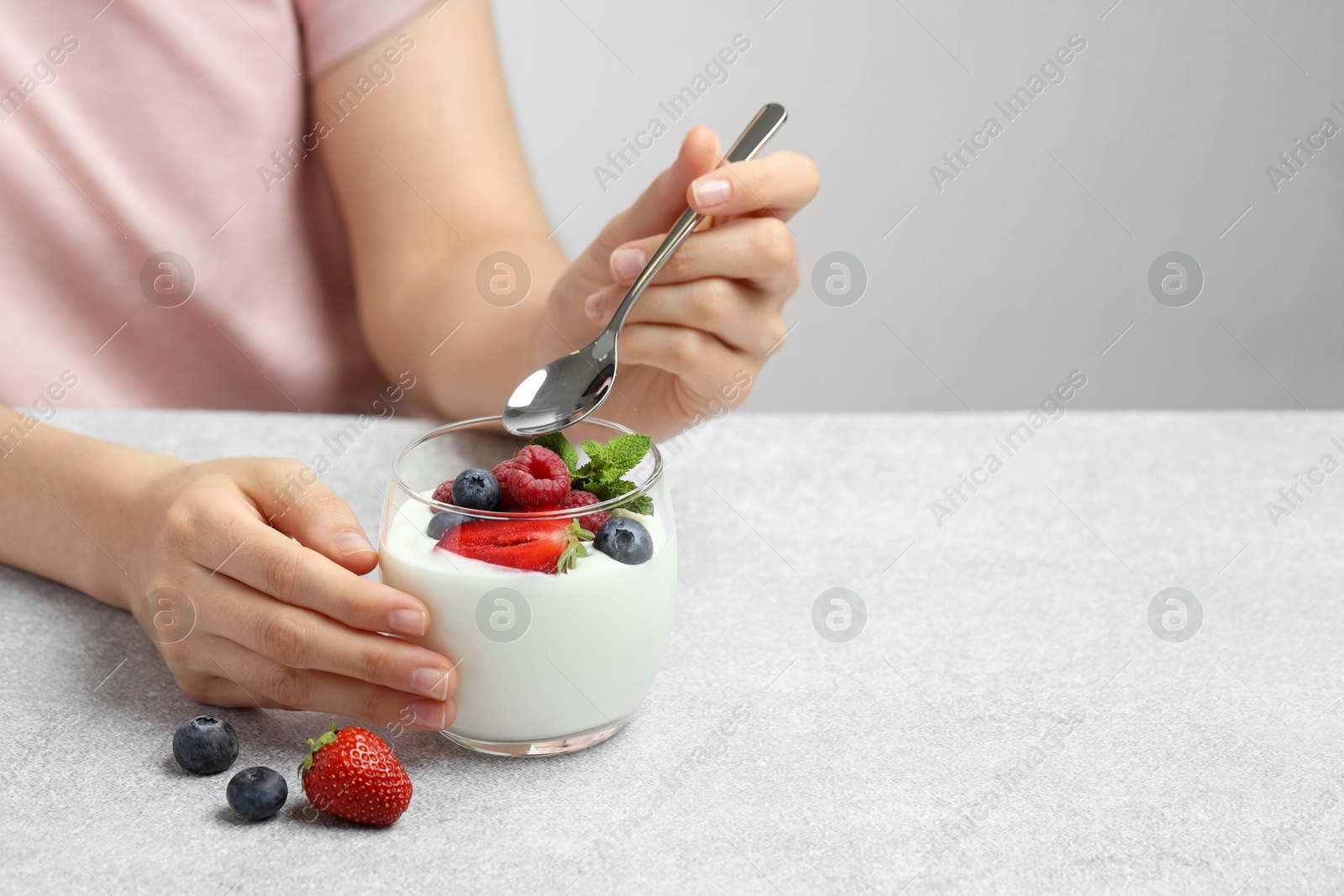 Photo of Woman eating tasty yogurt with fresh berries at light gray textured table, closeup. Space for text