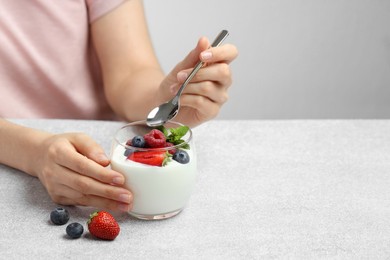 Photo of Woman eating tasty yogurt with fresh berries at light gray textured table, closeup. Space for text