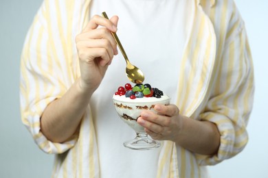 Photo of Woman eating tasty yogurt with fresh berries on light background, closeup