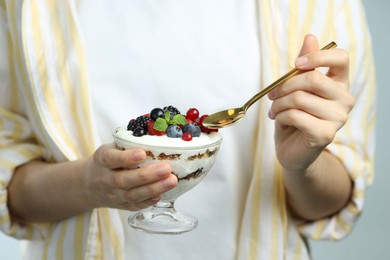 Photo of Woman eating tasty yogurt with fresh berries on light background, closeup