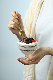 Woman eating tasty yogurt with fresh berries on light background, closeup