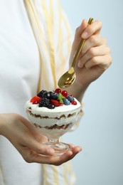 Woman eating tasty yogurt with fresh berries on light background, closeup