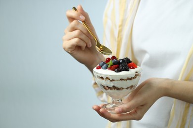 Woman eating tasty yogurt with fresh berries on light background, closeup. Space for text