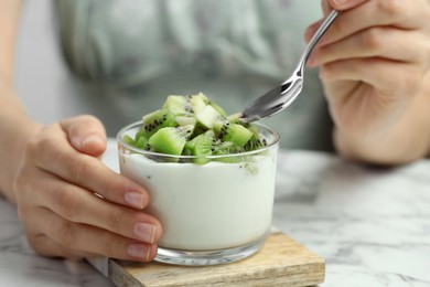 Woman eating tasty yogurt with fresh kiwi at white marble table, closeup