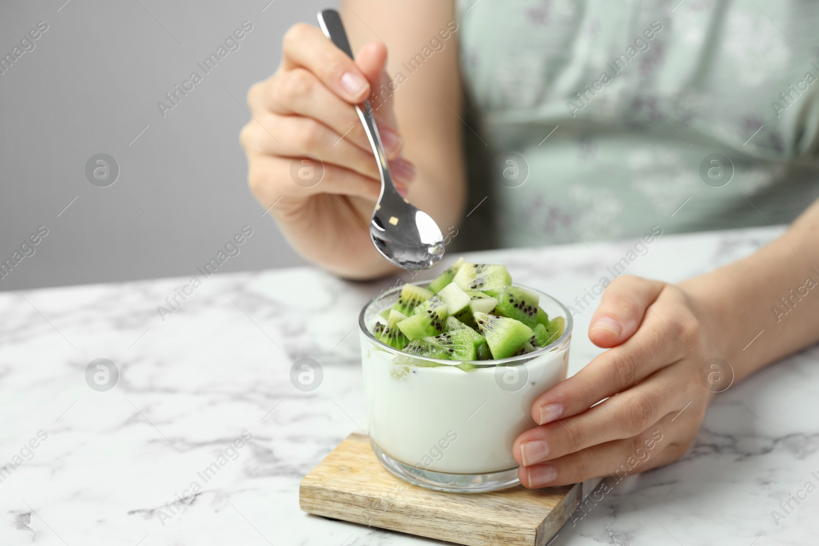 Photo of Woman eating tasty yogurt with fresh kiwi at white marble table, closeup. Space for text