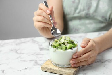 Photo of Woman eating tasty yogurt with fresh kiwi at white marble table, closeup. Space for text