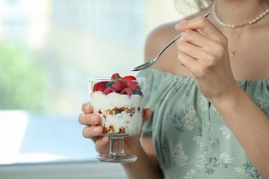 Woman eating tasty yogurt with fresh berries and granola indoors, closeup. Space for text