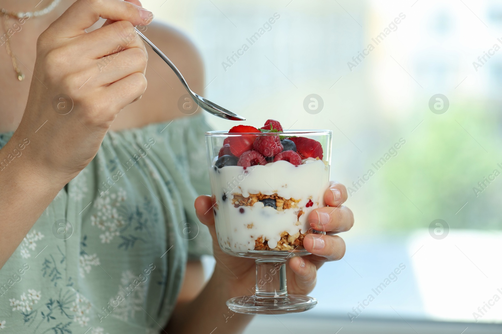 Photo of Woman eating tasty yogurt with fresh berries and granola indoors, closeup. Space for text